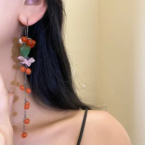Detailansicht der langen Quastenohrringe mit roten Beeren und grünen Blättern am Model.