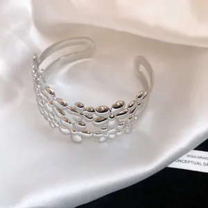 Close-up detail view of elegant silver floral metal cuff bracelet on white silk background