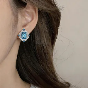 Close-up of vintage palace style stud earrings with blue rectangular zircon on ear.
