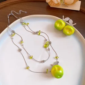 Close-up of double-layer beaded necklace and green resin apple earrings with zircon leaves