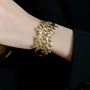 Detailed view of a gold-colored double-layer flower open cuff bracelet on a wrist.