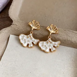 Close-up of elegant 14k gold plated ginkgo leaf earrings with sparkling zircons and white enamel