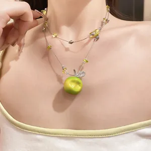 Detail of double-layer beaded necklace with green resin apple and zircon leaf pendant.