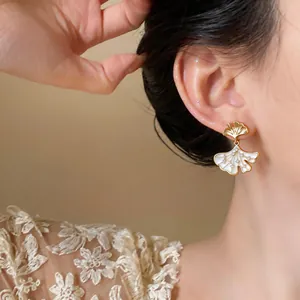 Detailed close-up of gold-plated ginkgo leaf earrings with zircon stones on model