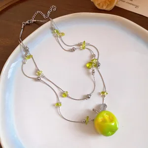 Detailed view of a double-layered necklace featuring a vibrant green resin apple pendant.