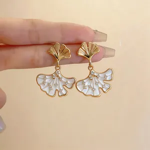Detail view of 14k gold-plated ginkgo leaf earrings with zircons and white enamel.
