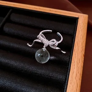 Elegant silver zircon bow open ring with a clear round resin bead on a black jewelry tray.