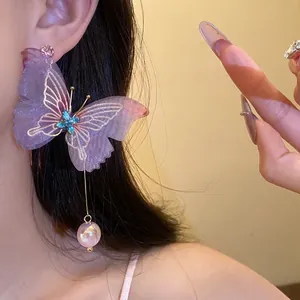 Elegantes pendientes largos de mariposa morada con perlas colgantes en una modelo
