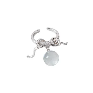 Elegant silver-toned bow ring with a zircon-studded center and a clear resin ball drop.