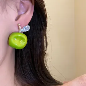 Detailed view of a green resin apple earring with a sparkling zircon leaf on a model's ear