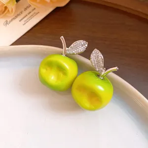 Detail view of green resin apple earrings with cubic zirconia leaves on a plate.
