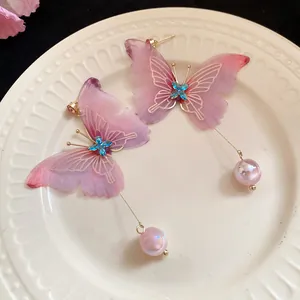 Detalle de pendientes de mariposa de colores con cristales azules y perlas.