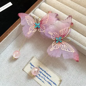 Detalle de pendientes de mariposa rosa con cristales azules y cadenas doradas