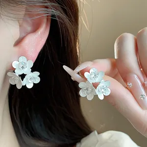 Detail shot of elegant white enamel flower stud earrings with sparkling crystals