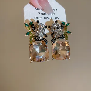 Primer plano de pendientes de panda con pedrería y piedras cuadradas color champán.