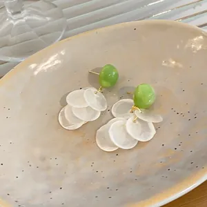 Primer plano de pendientes con borlas de concha blanca y perla verde en bandeja crema