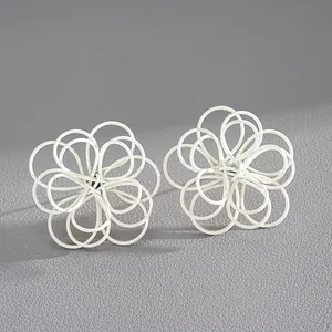 Vista detallada de pendientes de flores huecas pintados de blanco con diseño entrelazado