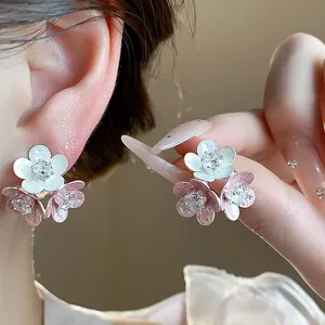 Close-up of pink and white enamel flower stud earrings with sparkling zircon centers.