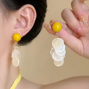 Detalle de pendientes de flecos de concha de verano con cuenta amarilla y pétalos