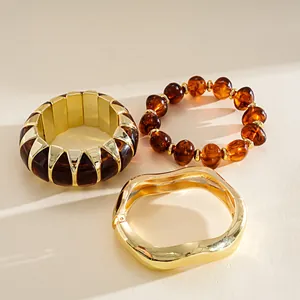 Detailed view of amber acrylic and gold metal bracelet set on beige surface