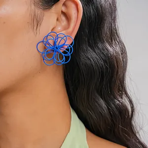 Primer plano de un pendiente de flor hueca azul vibrante usado en la oreja del modelo