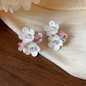 Close-up of elegant floral stud earrings with white and pink petals and zircon center