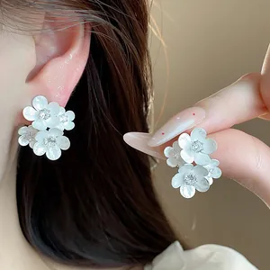Close-up of matte white floral stud earrings with sparkling zircon crystals on ear