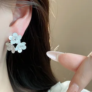 Detailed view of white triple flower stud earrings with sparkling zircon centers on ear