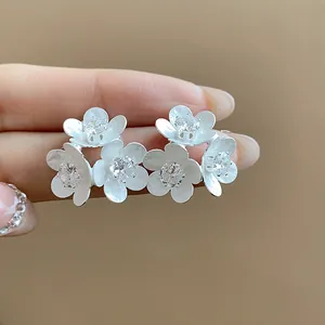 Close-up of elegant white enamel flower stud earrings with sparkling zircon centers