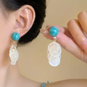 Detalle de pendientes con cuenta turquesa y borlas de concha blanca en una modelo