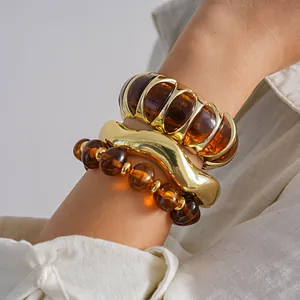 Macro detail of amber resin beads and polished golden metal bangles on a wrist.