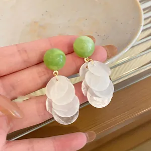 Primer plano de pendientes de concha estilo veraniego con cuentas verdes y discos blancos