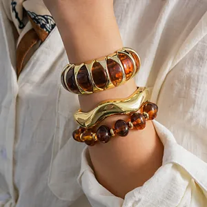 Retro amber acrylic and chunky gold bangle set styled on a white linen shirt cuff
