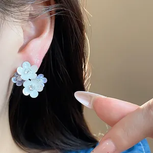 Close-up of white and blue enamel flower stud earrings with zircon centers on ear