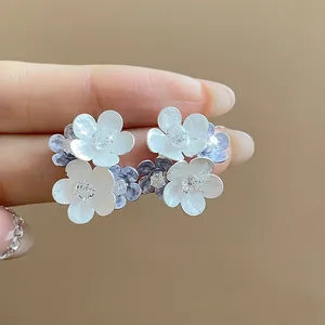 Close-up detail of white and blue flower stud earrings with sparkling zircon centers