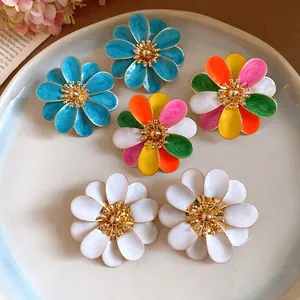 Primo piano di orecchini a lobo a forma di fiore in smalto colorato su un piatto ceramico