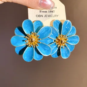 Dettaglio ravvicinato di orecchini a lobo a forma di fiore in smalto blu con stami dorati