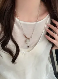 Detail view of a silver heart-shaped beaded necklace on a model wearing a white top.