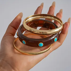Macro view of three-piece vintage resin and polished gold-toned bangles held in hand