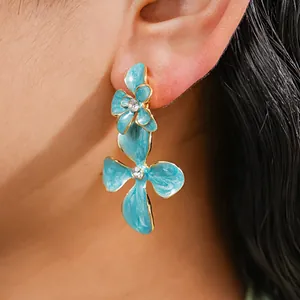 Gros plan de boucles d'oreilles fleur en émail bleu avec strass brillants sur l'oreille.