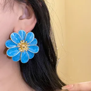 Primo piano di un orecchino a fiore in smalto blu indossato sull'orecchio di una modella