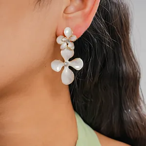 Gros plan détaillé d'une boucle d'oreille fleur en émail blanc avec un centre en strass.