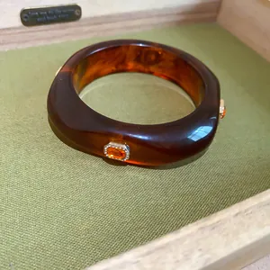 Close-up detail of chunky amber resin bangle featuring faceted orange rhinestone accents