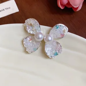 Macro detail of butterfly stud earrings with crushed stones and pearls on cream plate