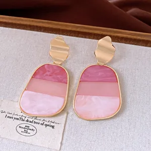 Primo piano di orecchini vintage in marmo rosa con perni dorati ondulati su lino.