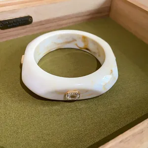 Macro view of marbled cream resin bangle with sparkling crystal detail on olive tray
