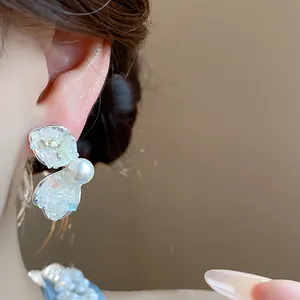 Close-up of silver wing-shaped earrings with crushed stones and a pearl