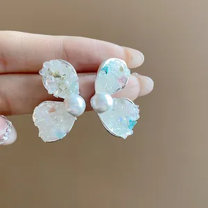 Detailed macro view of silver wing-shaped ear studs featuring crushed stones and pearls