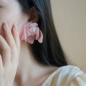 Vista detallada de un pendiente de flor de gasa rosa con perla en la oreja del modelo