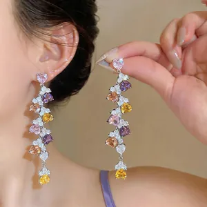 Close-up of colorful heart-shaped zircon dangle earrings with tassels.